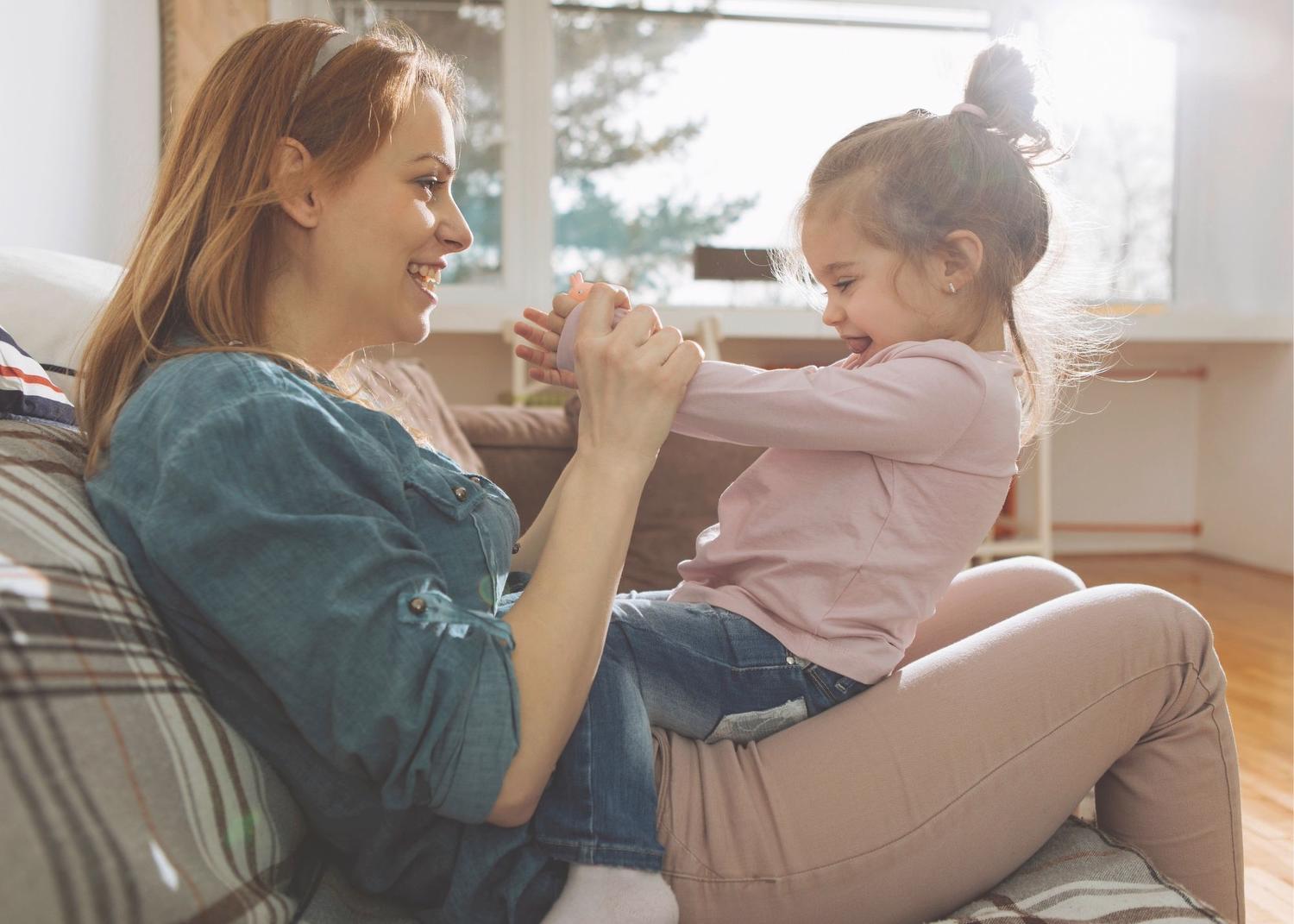 Woman sitting with young girl on her lap facing each other smiling and holding hands