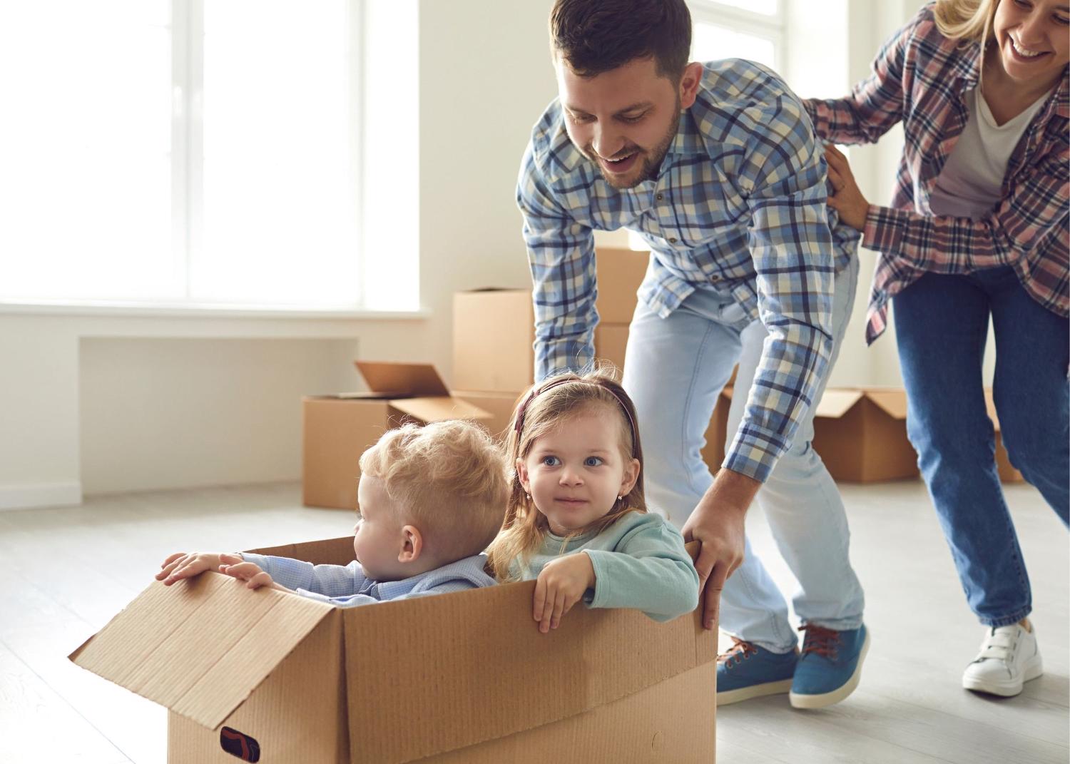 Two young children sitting in a cardboard box getting pushed by a man and woman smiling