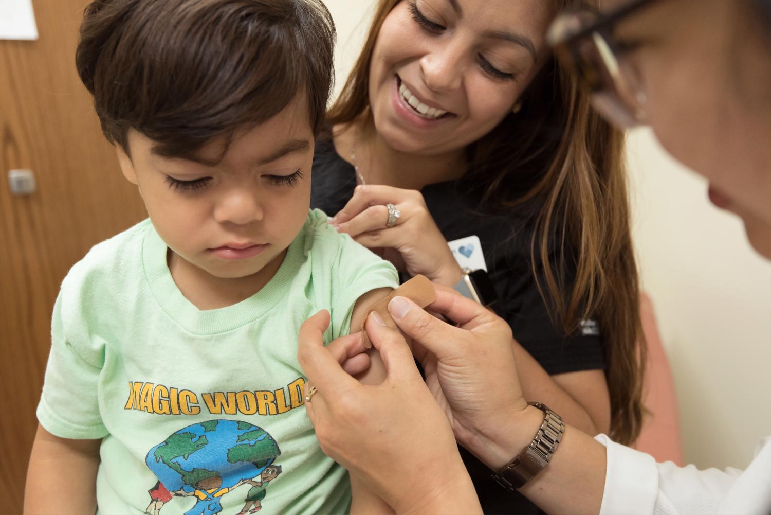 A young child sits on smiling woman's lap as a nurse puts a band aid on their arm..