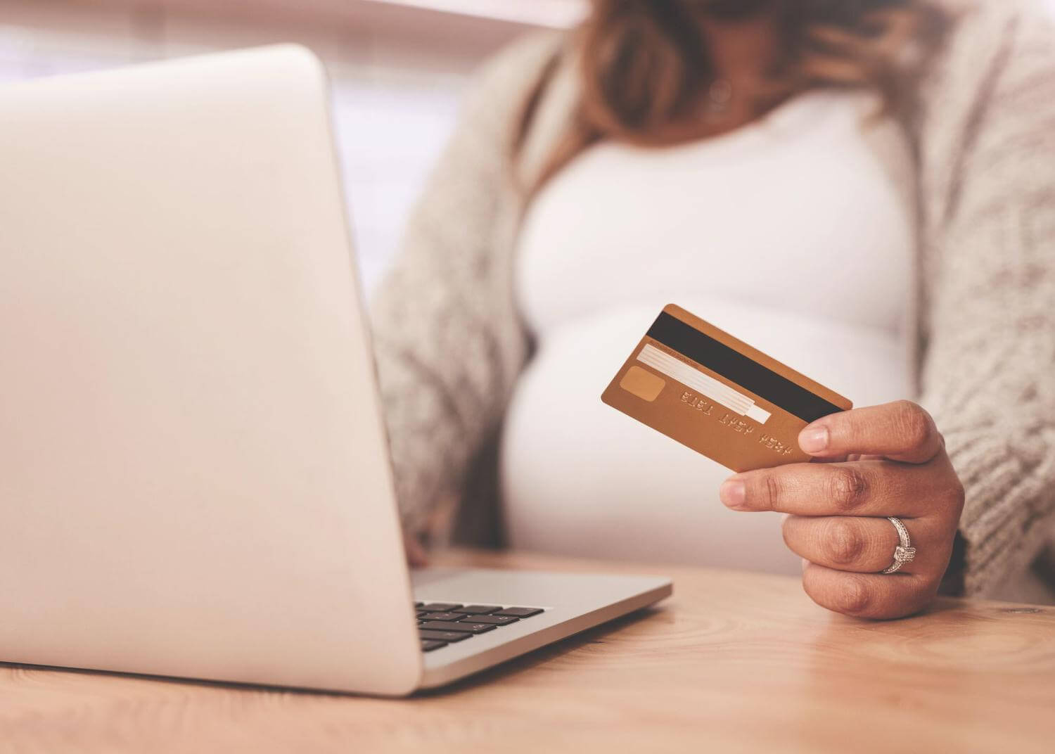 Open laptop with pregnant woman sitting, credit card in hand