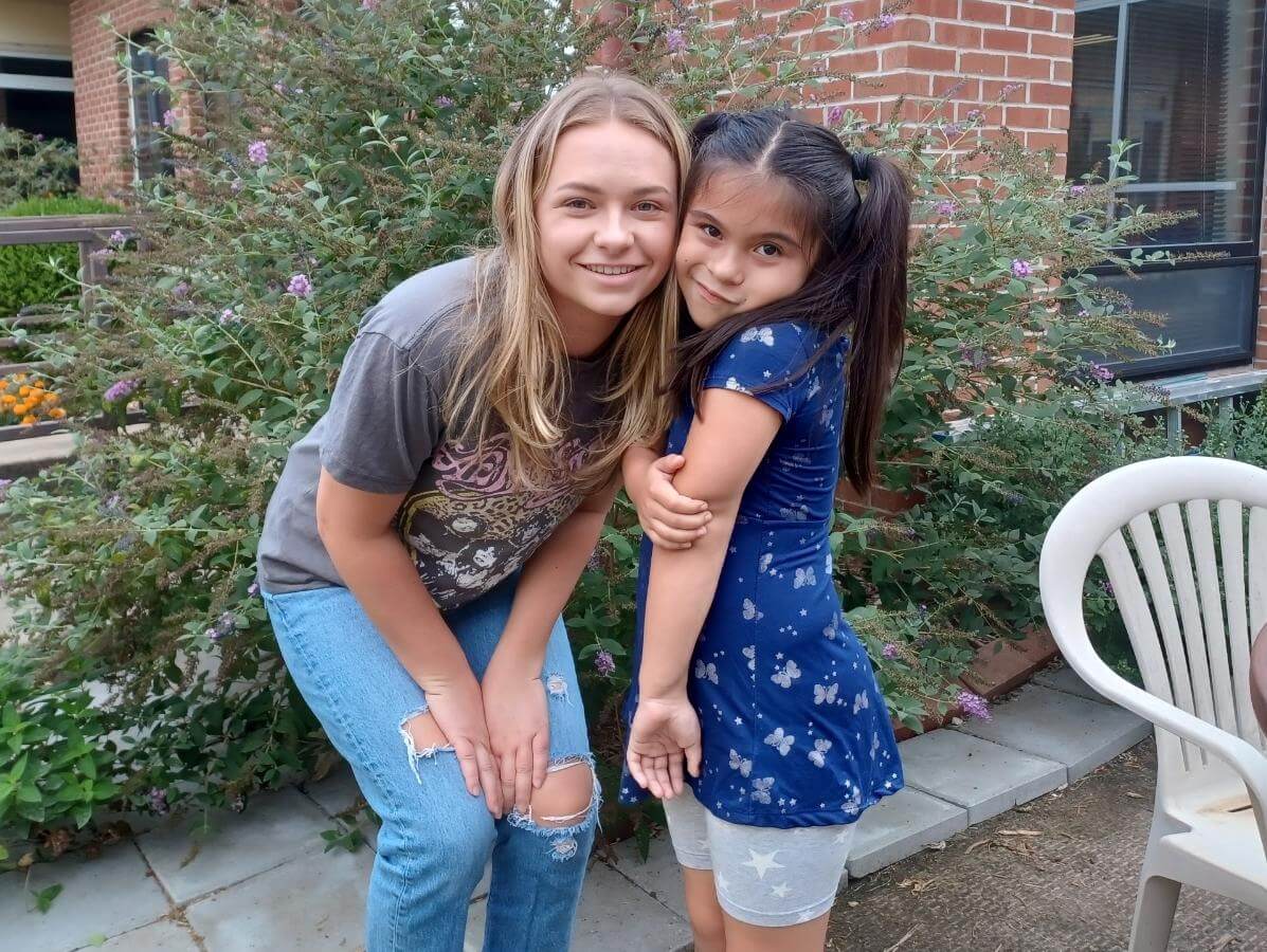 Young woman leaning down cheek-to-cheek with young girl, both smiling