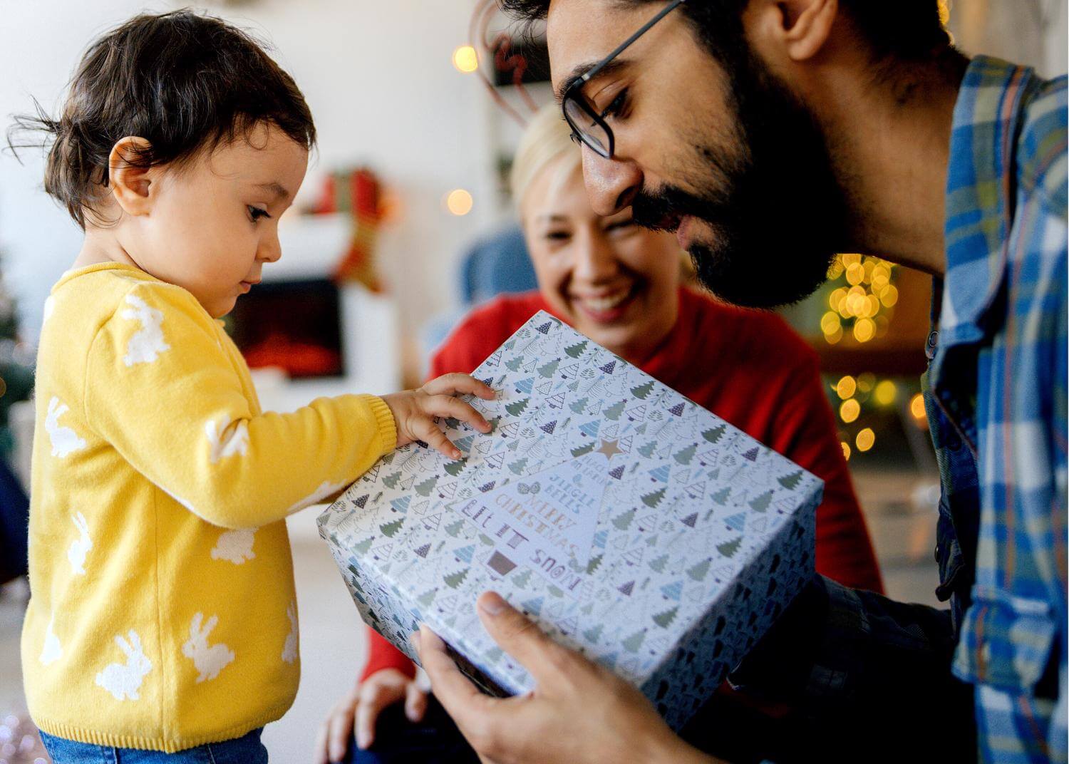 Toddler in a yellow sweater receives wrapped gift from fatherly figure