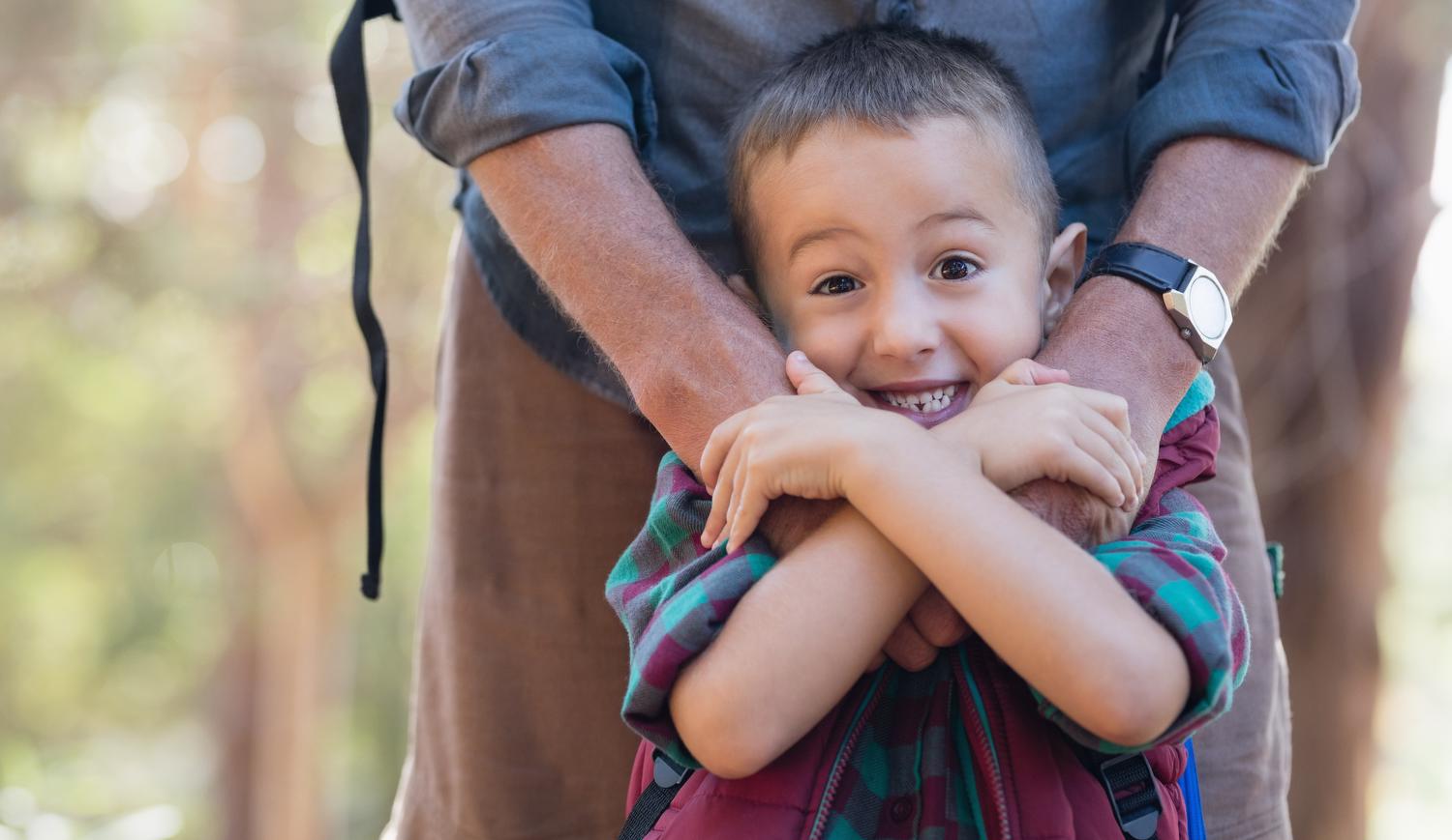 Boy smiling and squeezing adult's hands on his shoulders