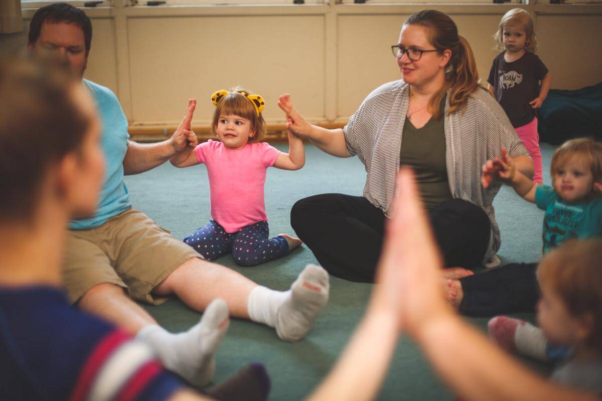 Young girl sitting between a man and a woman, hands raised with palms touching each other