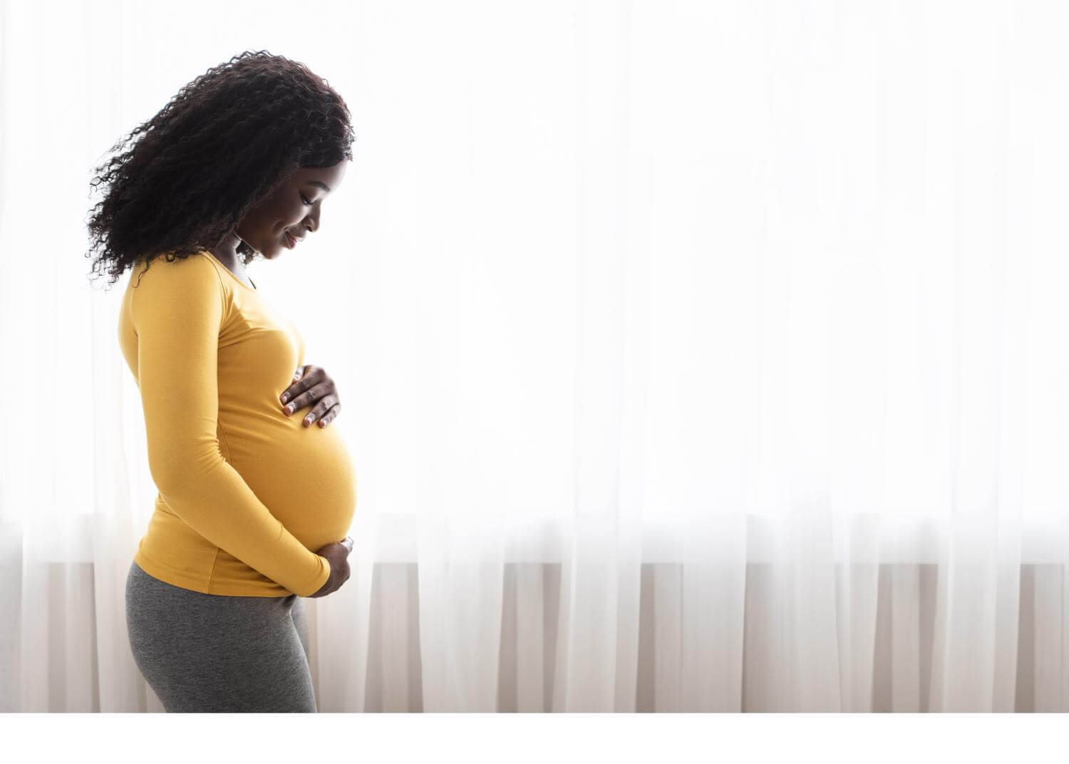 Black pregnant woman turned to the side, hands encircling stomach