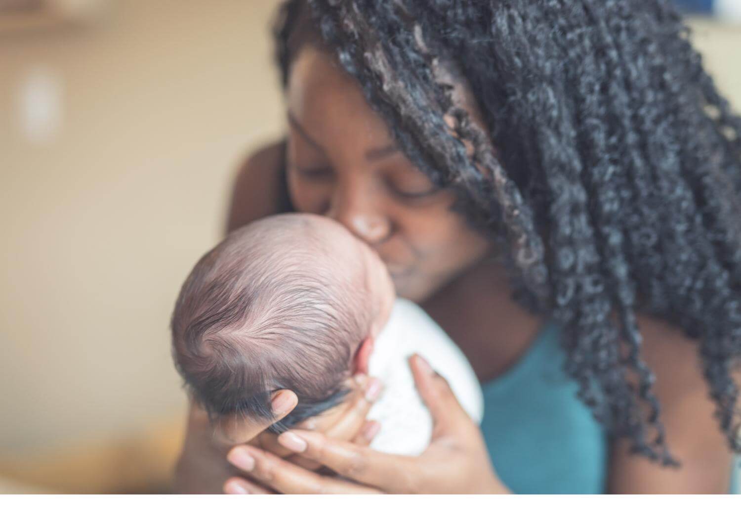 Woman of color with long hair, kissing newborn baby
