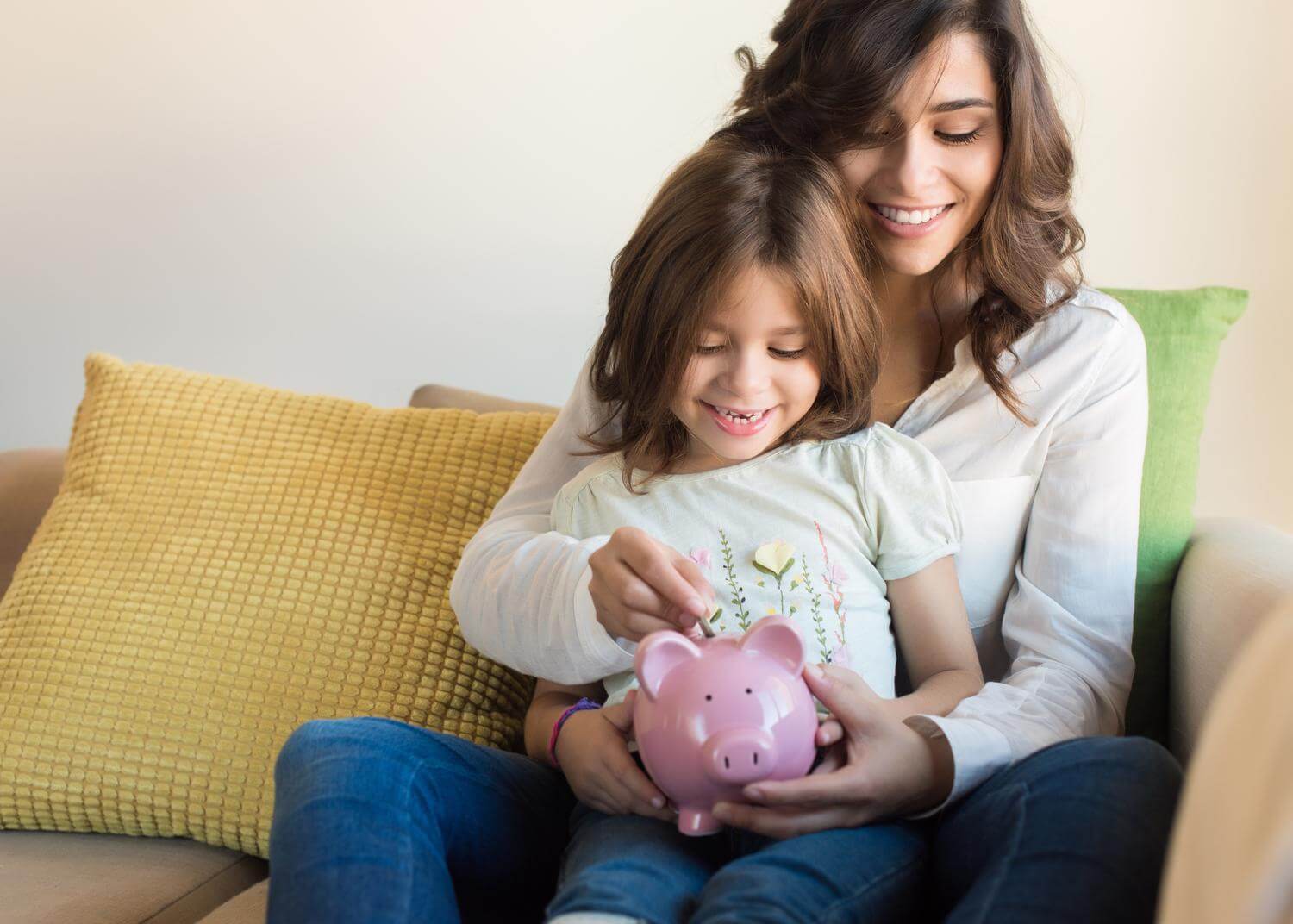 Mom and young daughter, smiling, holding a pink piggy bank