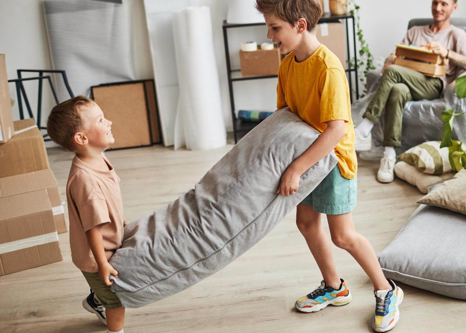 Two young boys carrying a large pillow, smiling