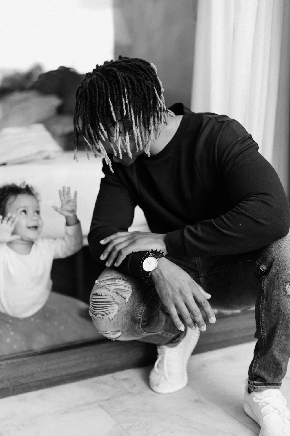 A toddler aged girl is communicating with an adult male using her hands and smiling.  He is kneeling down and giving her his full attention.