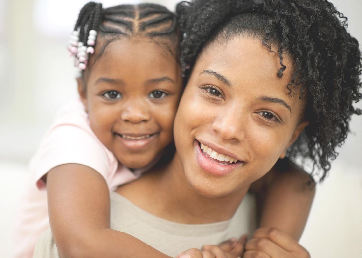 Young girl hugging woman from behind with arms around her neck and both are smiling