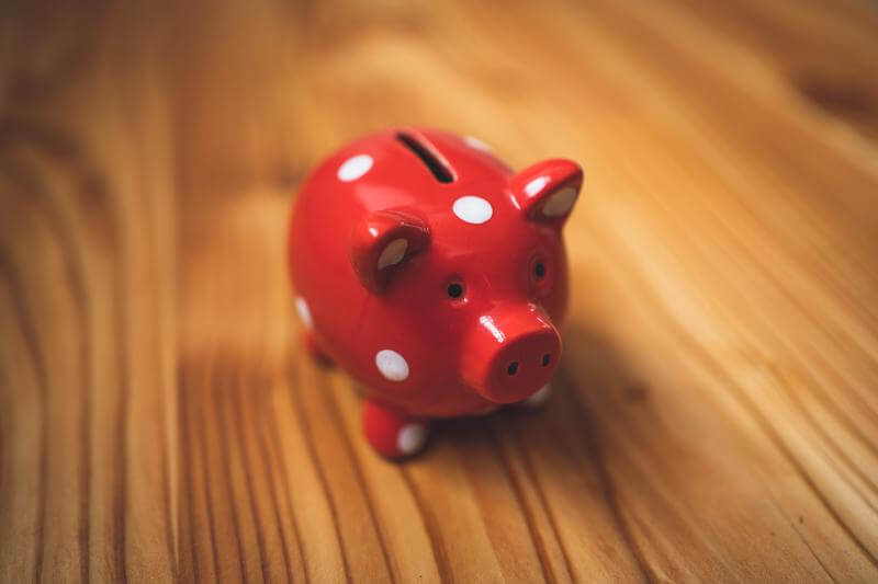 A red and white polka dotted piggy bank sits on a wooden table.