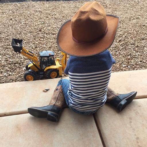 Young child wearing a cowboy hat, sitting with legs in a W-shape out to each side