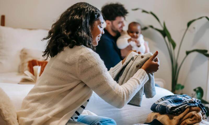 Woman looking at clothes with man holding baby in background