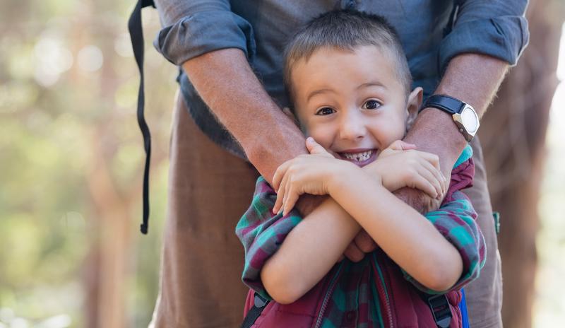 Boy smiling and squeezing adult's hands on his shoulders