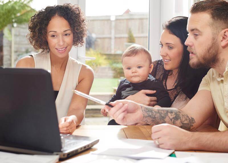 Couple with infant looking at laptop with a woman, possibly financial advisor