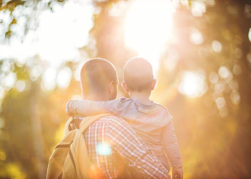 Father holding child outside with sun shining through branches